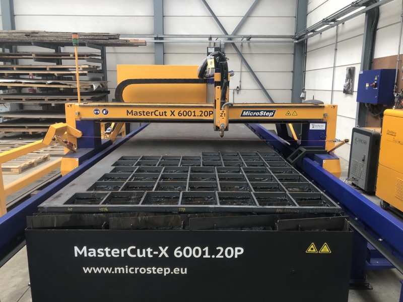 Gele CNC-plasmasnijtafel van MicroStep in de werkplaats, met uitgesneden stalen raster op de tafel