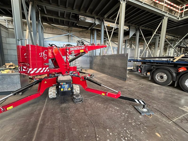 Rode compacte rupskraan van Constructie De Greyt met uitgeschoven steunpoten in een hal